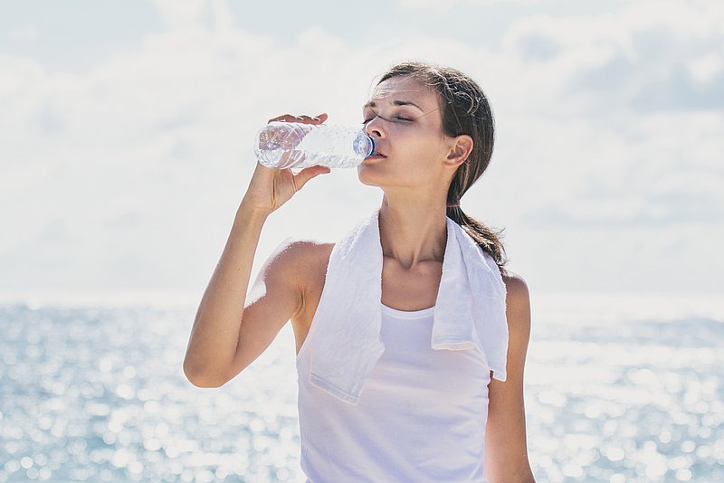 Eine Frau löscht ihren Durst mit natürlichem Mineralwasser an einem heißen Sommertag.
