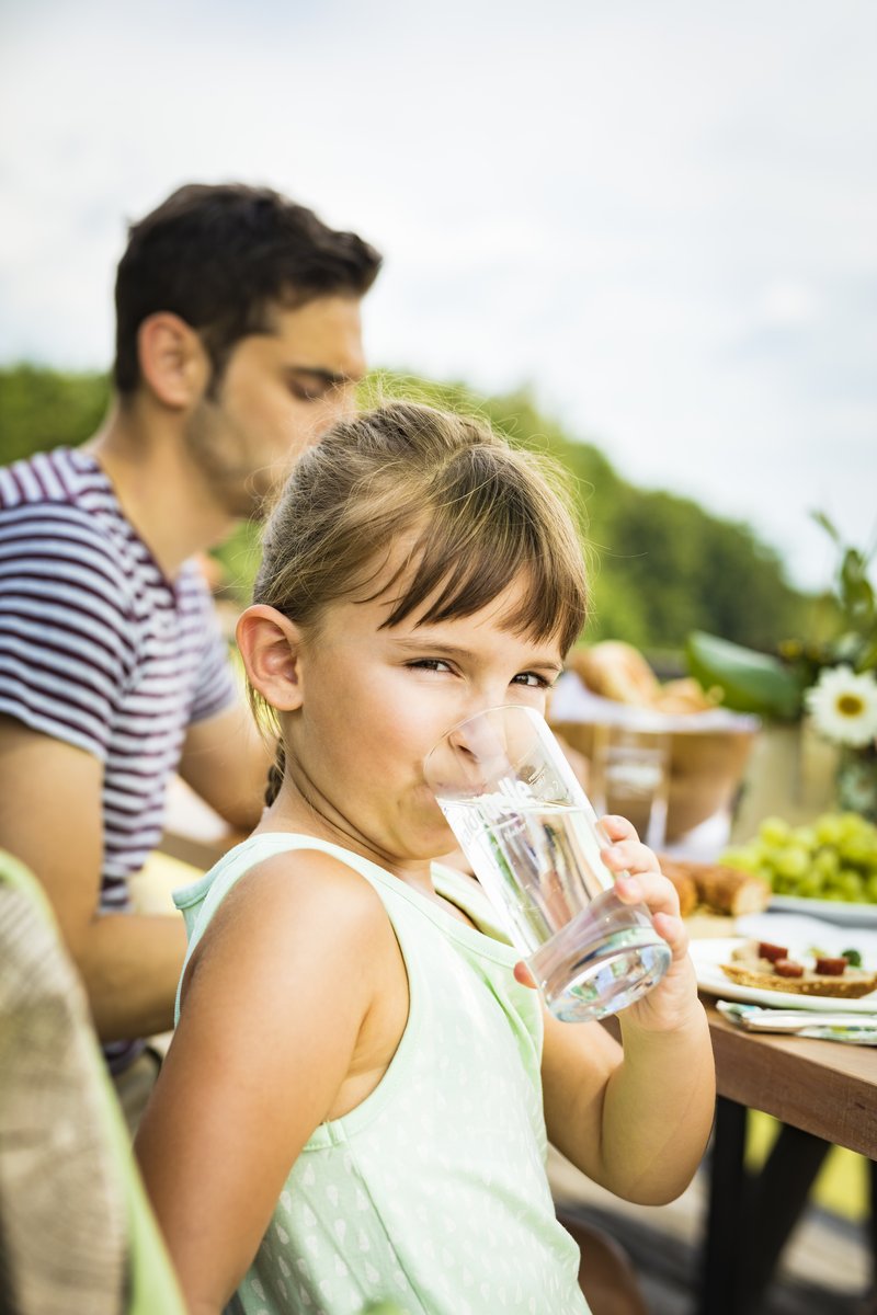 Auf einer Bank im Garten trinkt ein Mädchen natürliches Mineralwasser von Waldquelle.