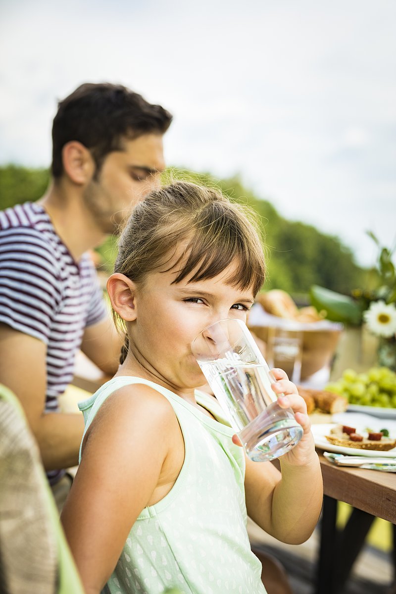 Foto: Marco Rossi Auf einer Bank im Garten trinkt ein Mädchen natürliches Mineralwasser von Waldquelle.