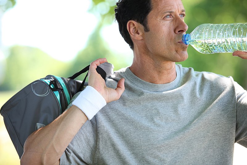 Ein Mann mit Sporttasche trinkt natürliches Mineralwasser.